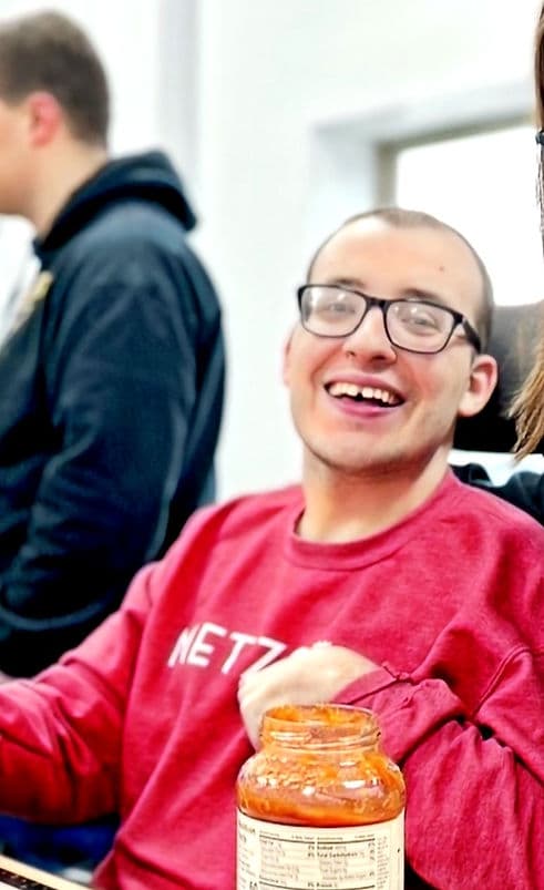 A man in a wheelchair sits and cooks using adaptive utensils